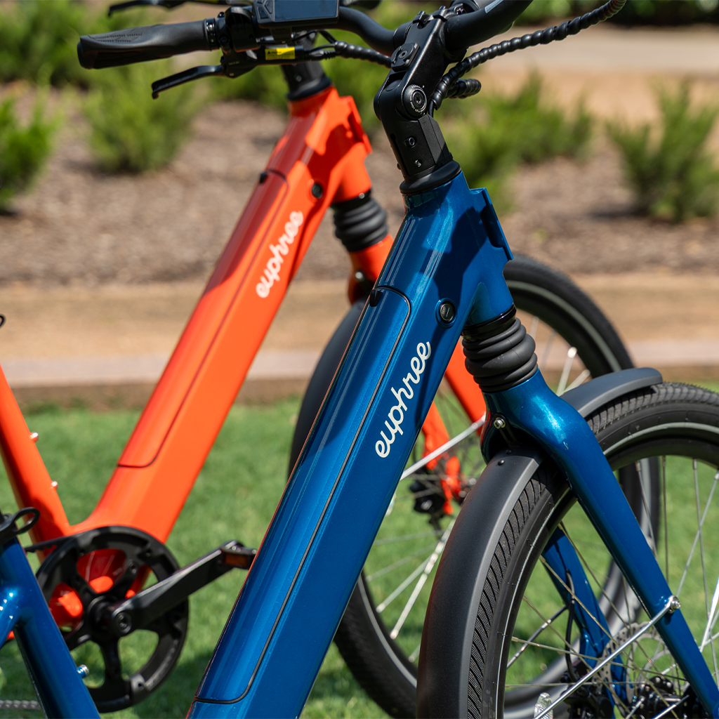 Close-up of Euphree Solar Sparrow bikes in Riviera Blue and Canyon Flame, highlighting the step-through frame and top-loading battery outdoors