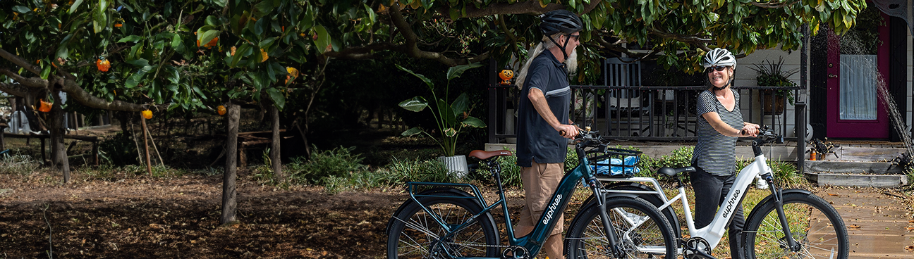 A couple walking alongside their two City Robin ebikes, enjoying the crisp fall weather with colorful leaves in the background.