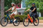 Couple riding Solar Sparrow electric bikes in Riviera Blue and Canyon Flame through a park trail